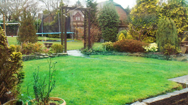 Sloped patio and steps leading up to a raised shed and gently curved lawn